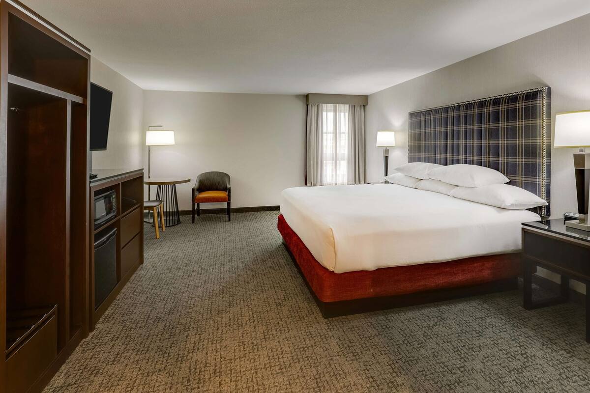 A hotel room with a large bed, a desk, a chair, a wardrobe, and a TV.