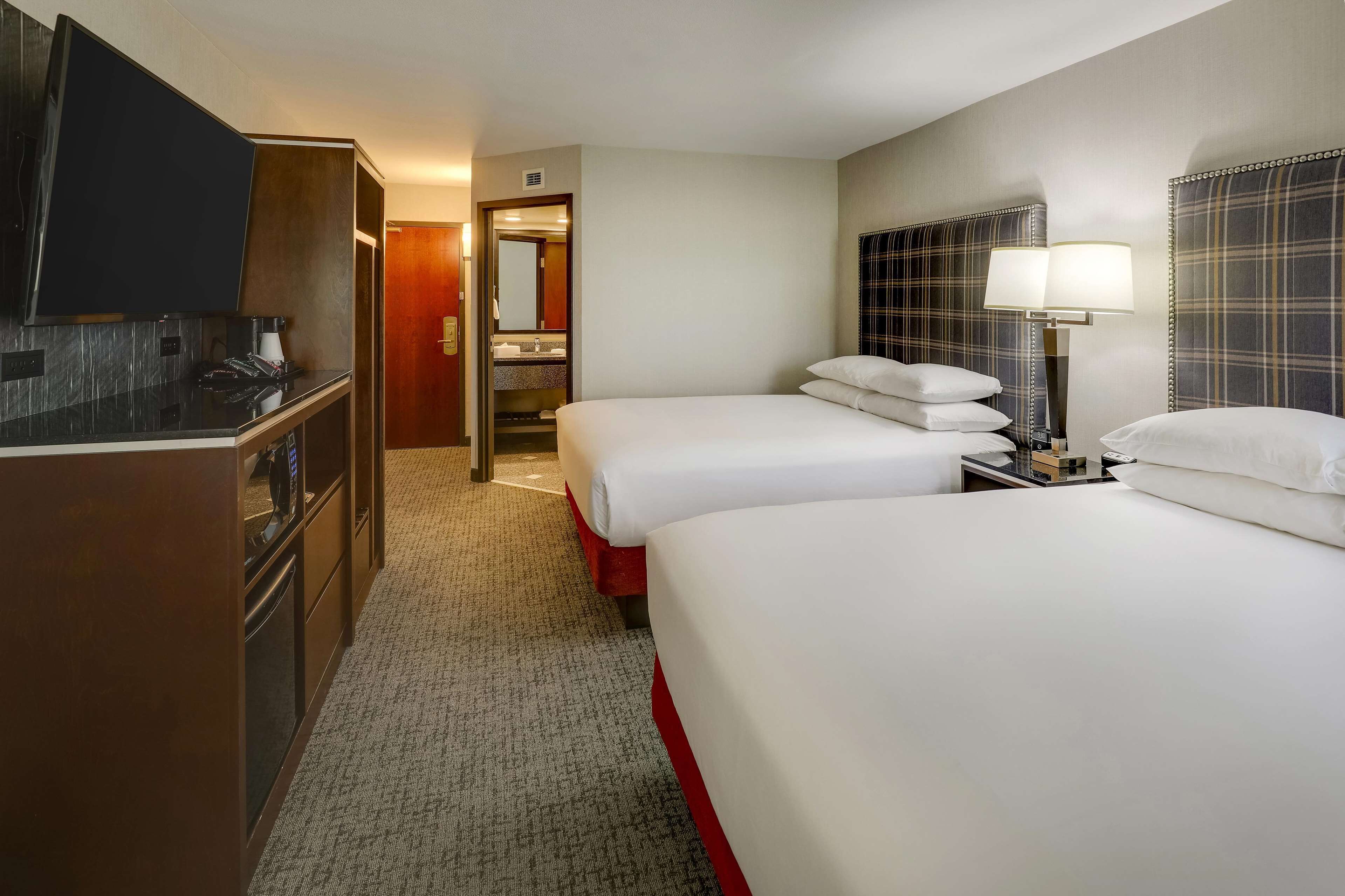 A hotel room with a large bed, a smaller bed, a desk with a flat-screen TV, a lamp, and a mirror.