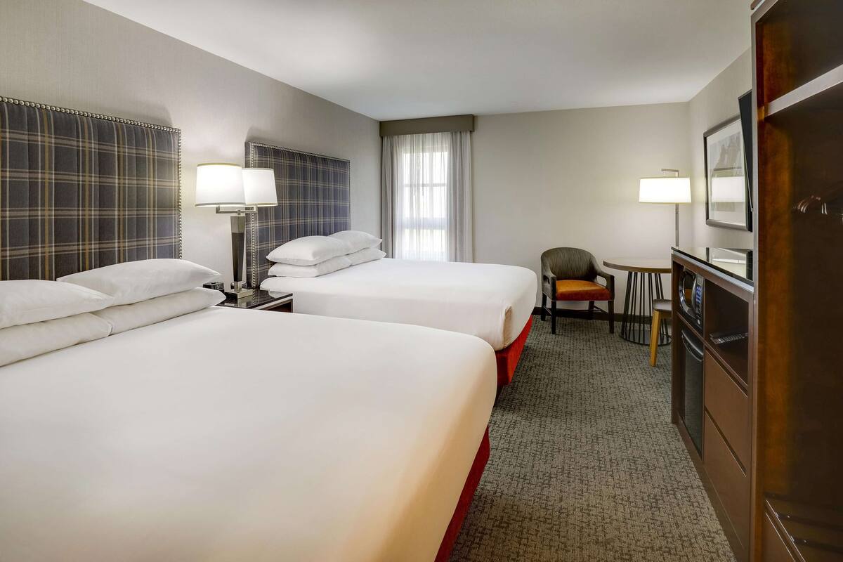 A hotel room with two beds, a desk, a chair, a small table, and a refrigerator.