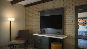 Una habitación con pared de ladrillo, un televisor de pantalla plana sobre un escritorio, una silla y una pequeña planta en maceta.