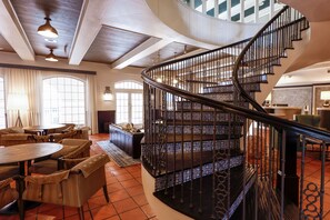 A spacious lobby with a curved staircase, a dining area with round tables and chairs, and large windows allowing natural light. - Casa De Palmas, Trademark Collection by Wyndham (McAllen)