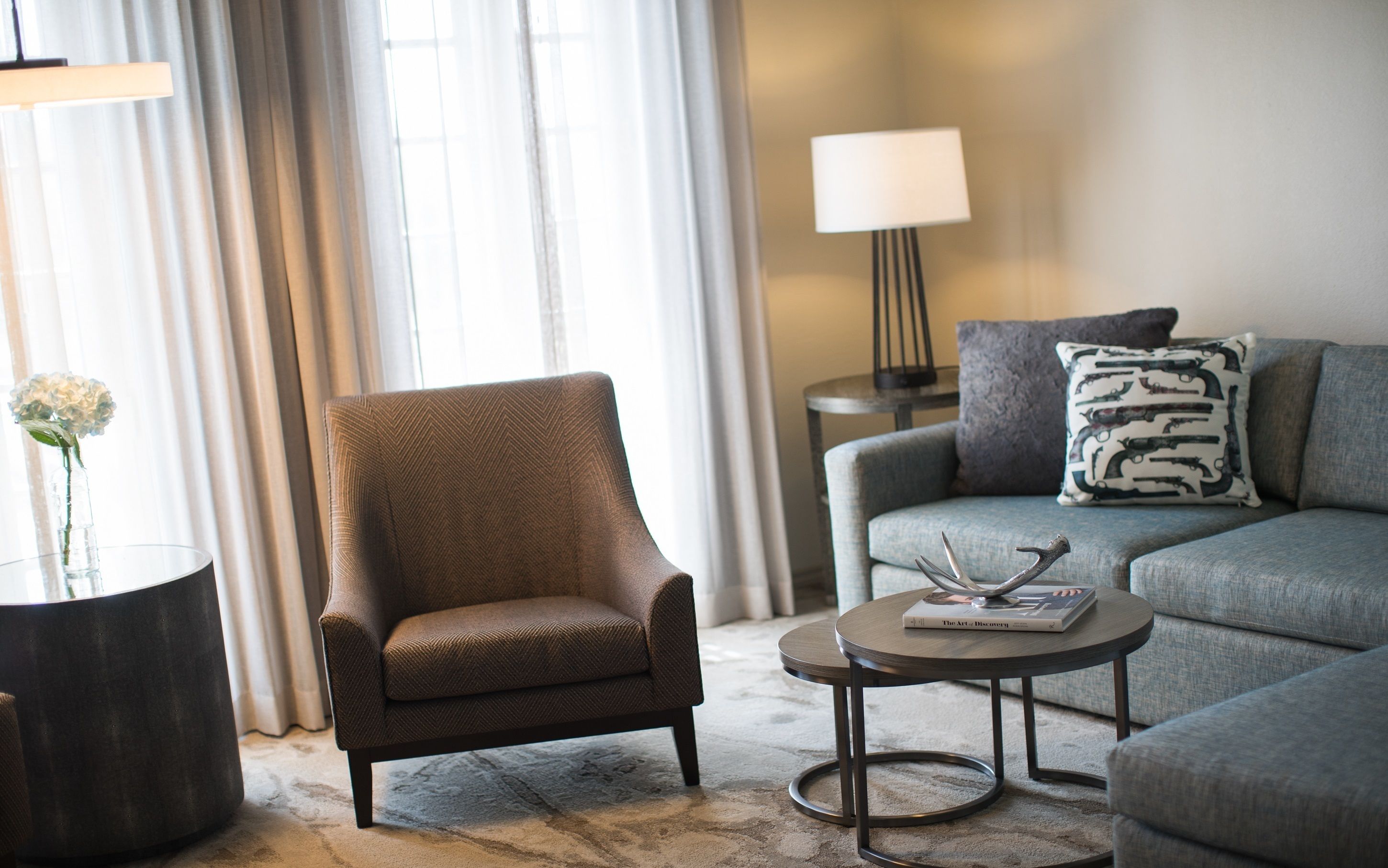 A modern living room with a brown armchair, grey sofa, and a small round table with a book.