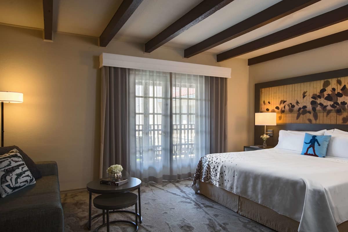 Una habitación de hotel con cama, sofá, una mesita y ventana con cortinas.