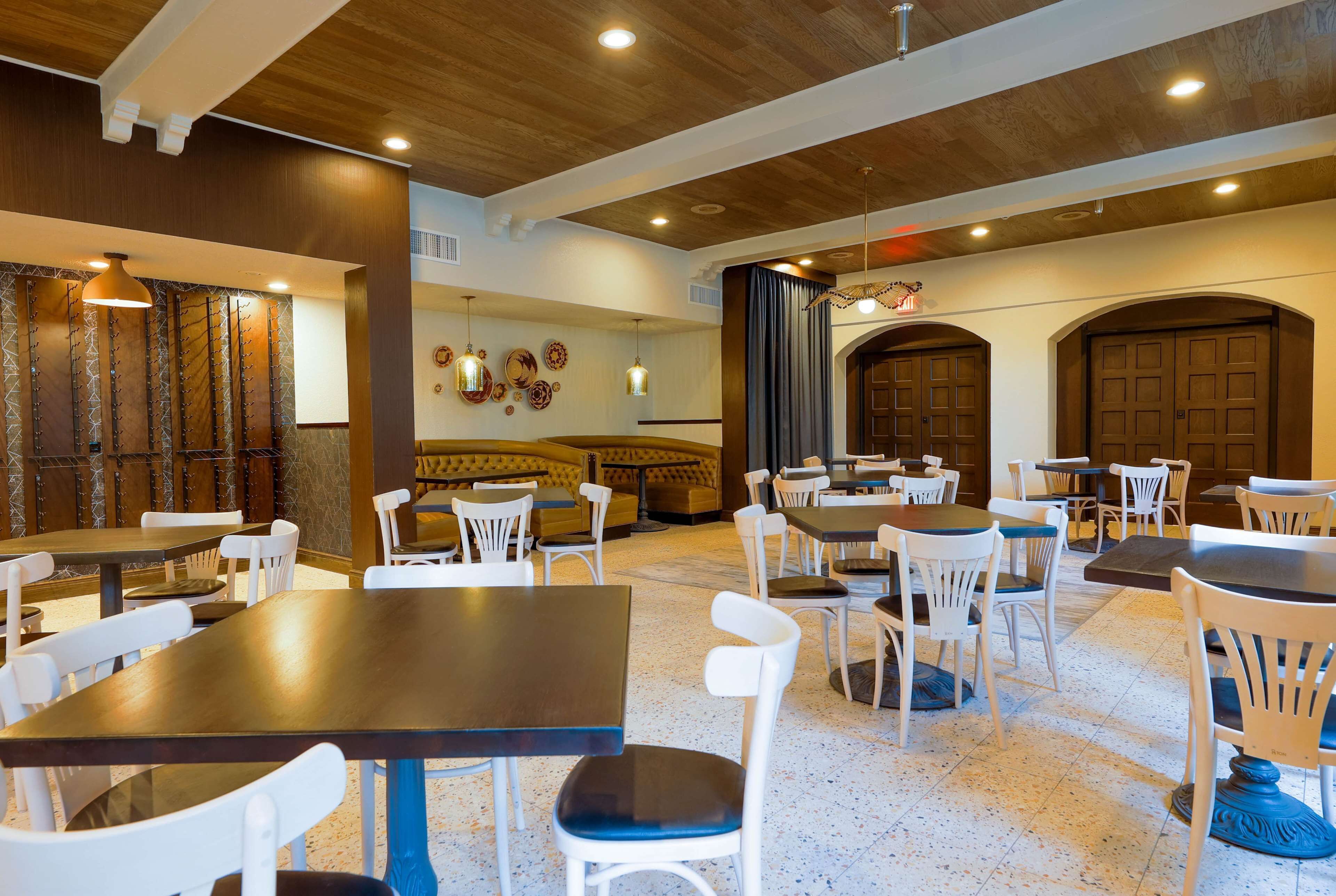 A spacious dining area with wooden tables and white chairs, a large cushioned bench, and a decorative wall with hanging lights.