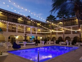 Un patio con piscina, luces colgantes, palmeras y mesas dispuestas para un evento.
