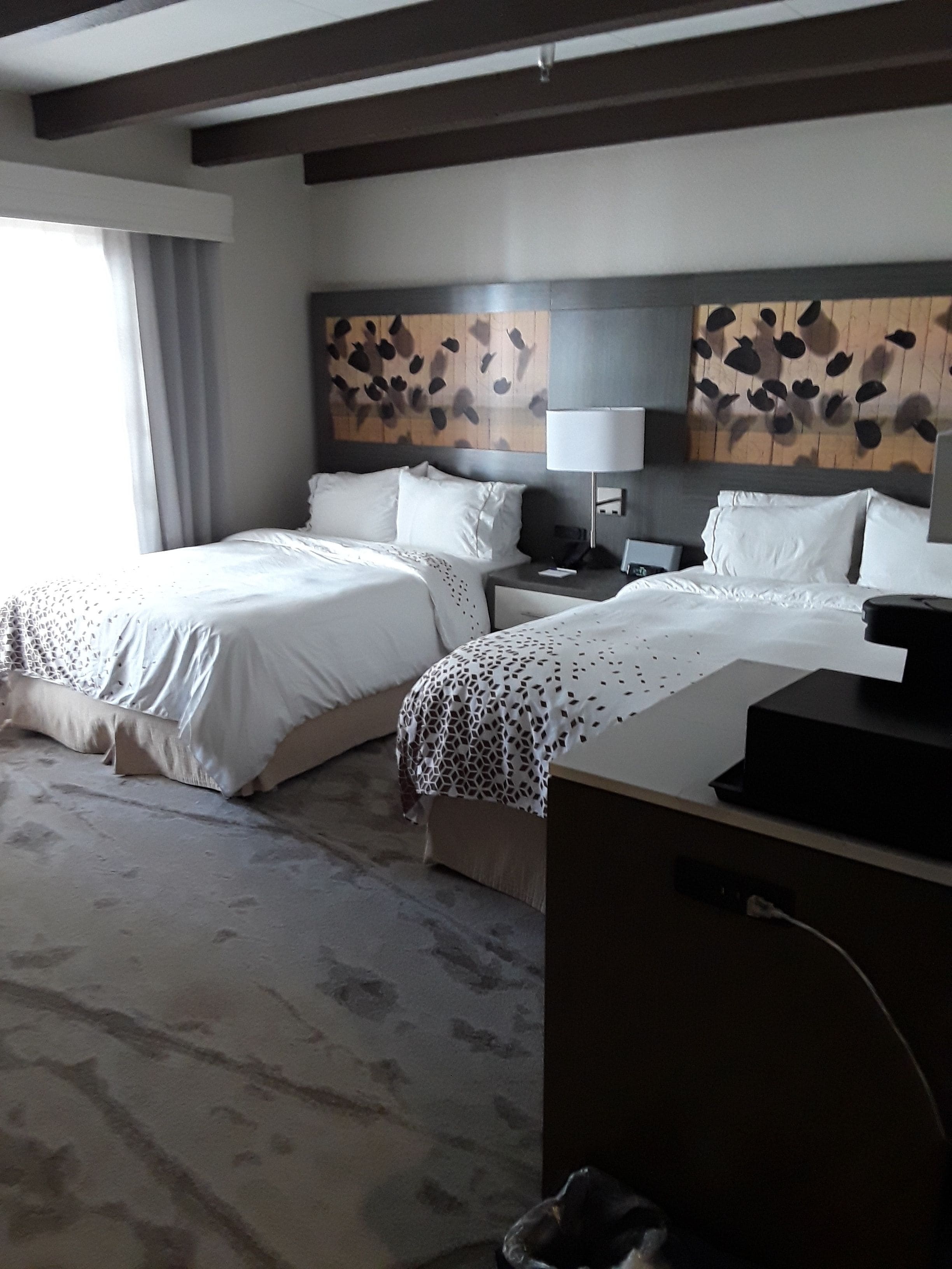 A hotel room with two beds, a desk, a lamp, and a decorative wall.