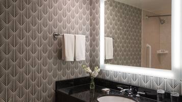 A bathroom with a patterned wallpaper, a black countertop, a round sink, a mirror, and a shower area.