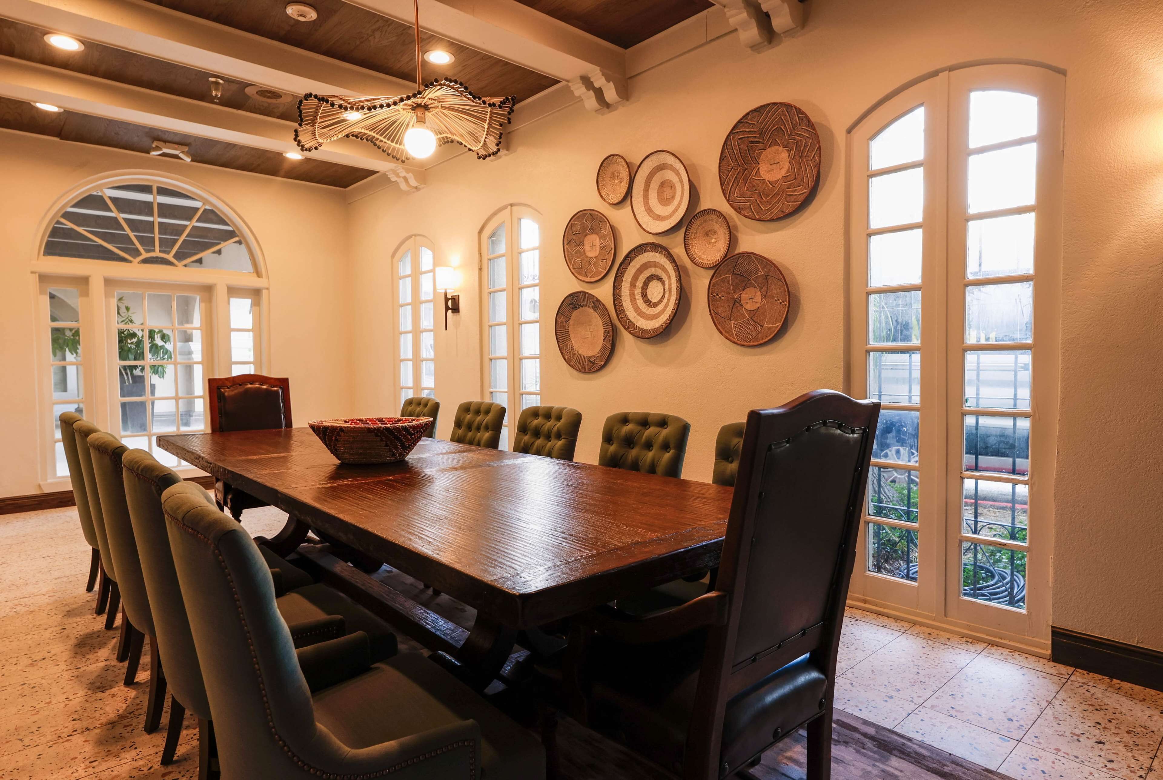 A dining area with a wooden table and upholstered chairs, surrounded by large windows and decorative wall art.