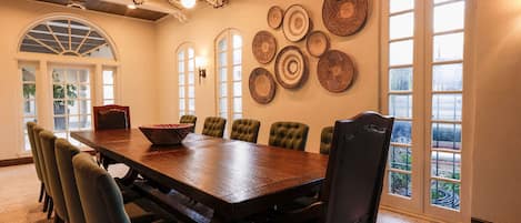 A dining area with a wooden table and upholstered chairs, surrounded by large windows and decorative wall art.