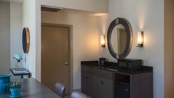 A dining area with a wooden table, chairs, a vase with flowers, a wall-mounted mirror, and a microwave on the counter.