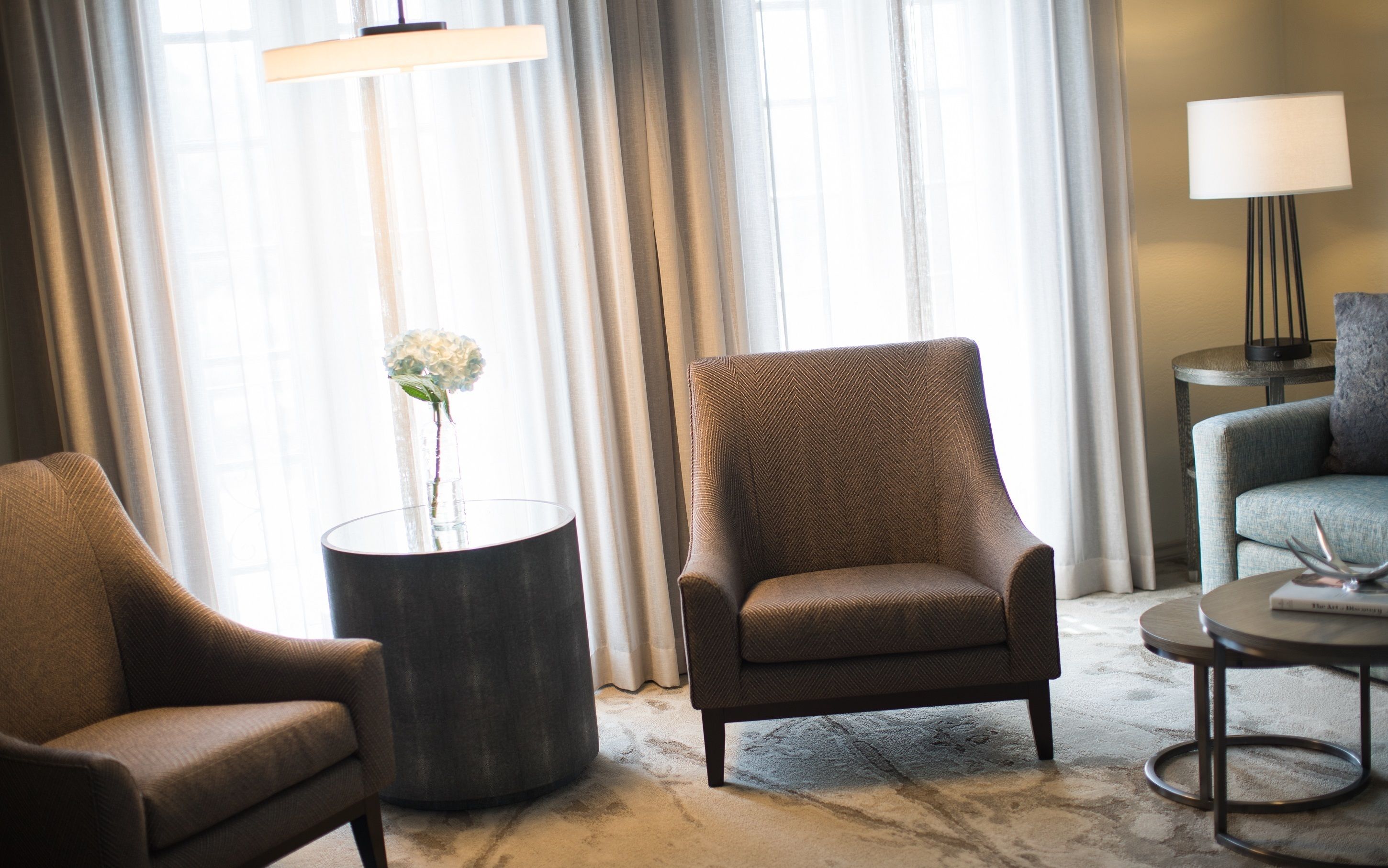 A room with a brown armchair, a round side table with a vase, and a lamp on a side table.