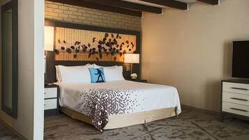 A hotel room with a large bed, a wooden headboard, a nightstand, a dresser, and a TV.
