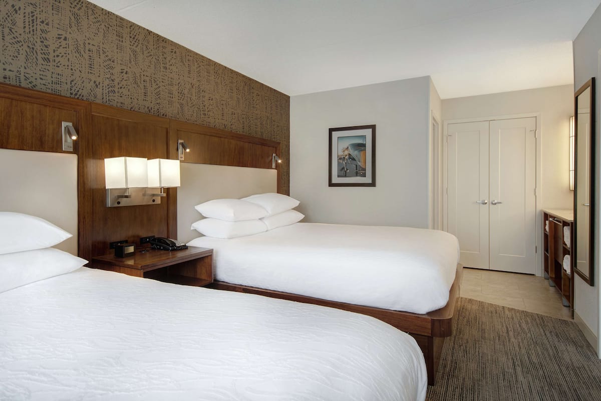 Ein Hotelzimmer mit zwei Betten, einem hölzernen Kopfteil, Nachttischlampen, einem gerahmten Bild an der Wand und einer weißen Tür.