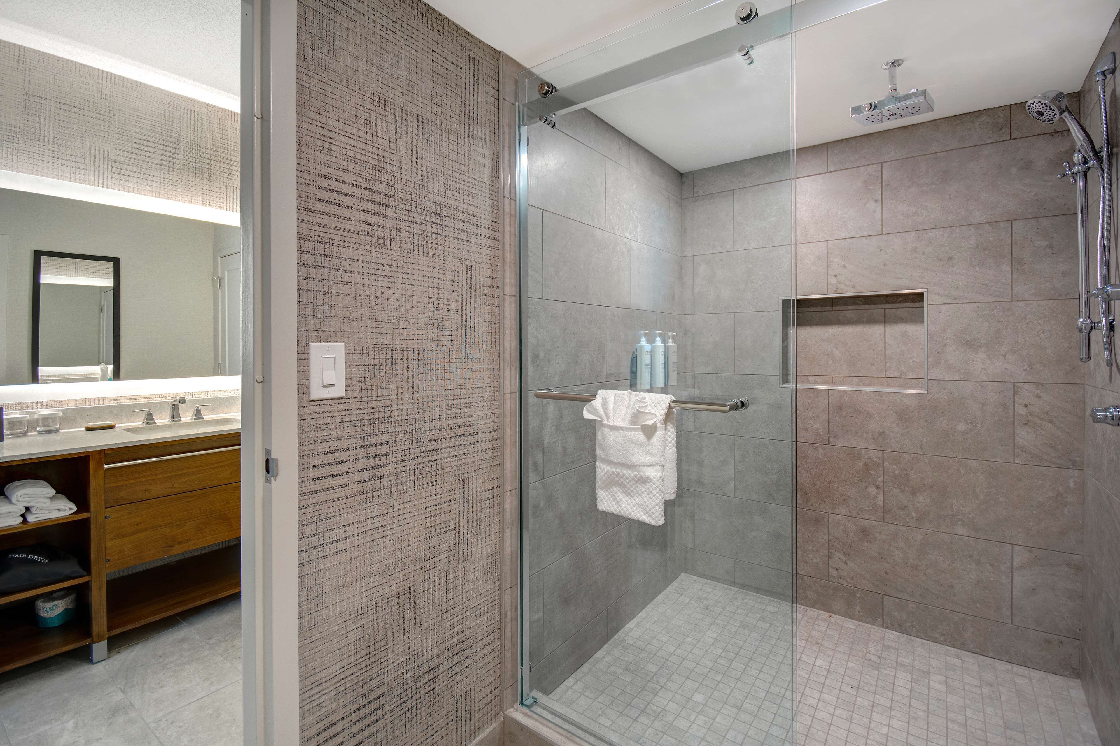 A modern bathroom with a glass-enclosed shower, a wooden vanity with a mirror, and neatly folded towels.