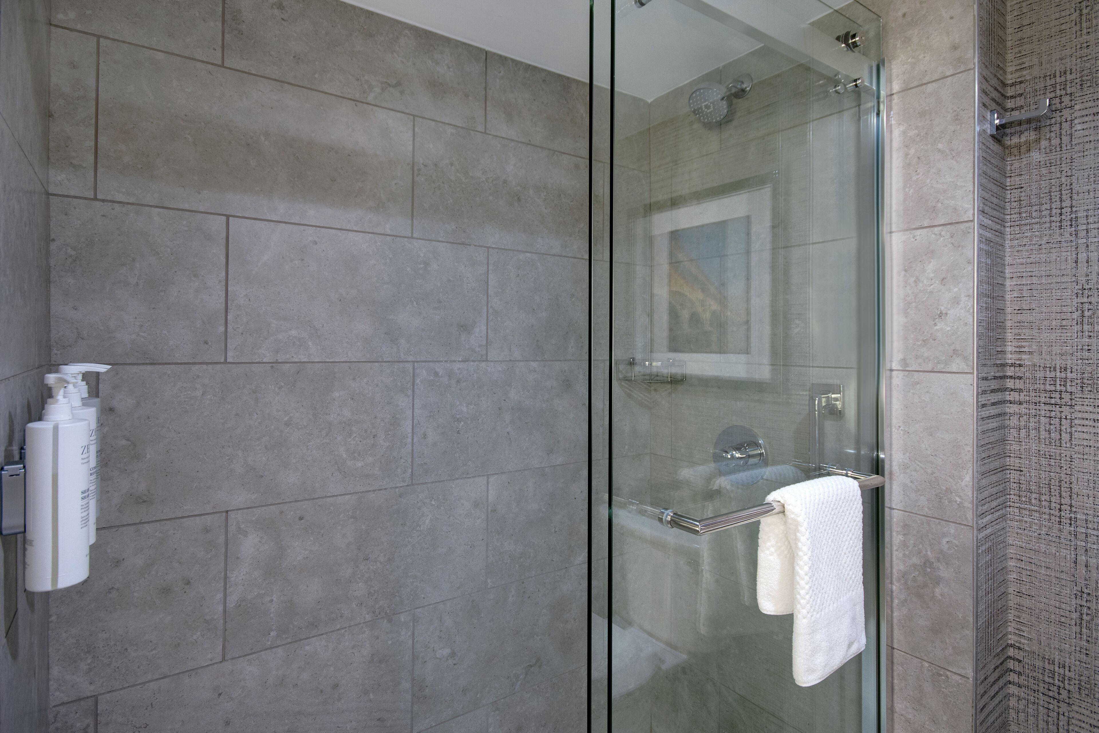 A modern bathroom with a glass shower enclosure, grey tiled walls, and a glass door.