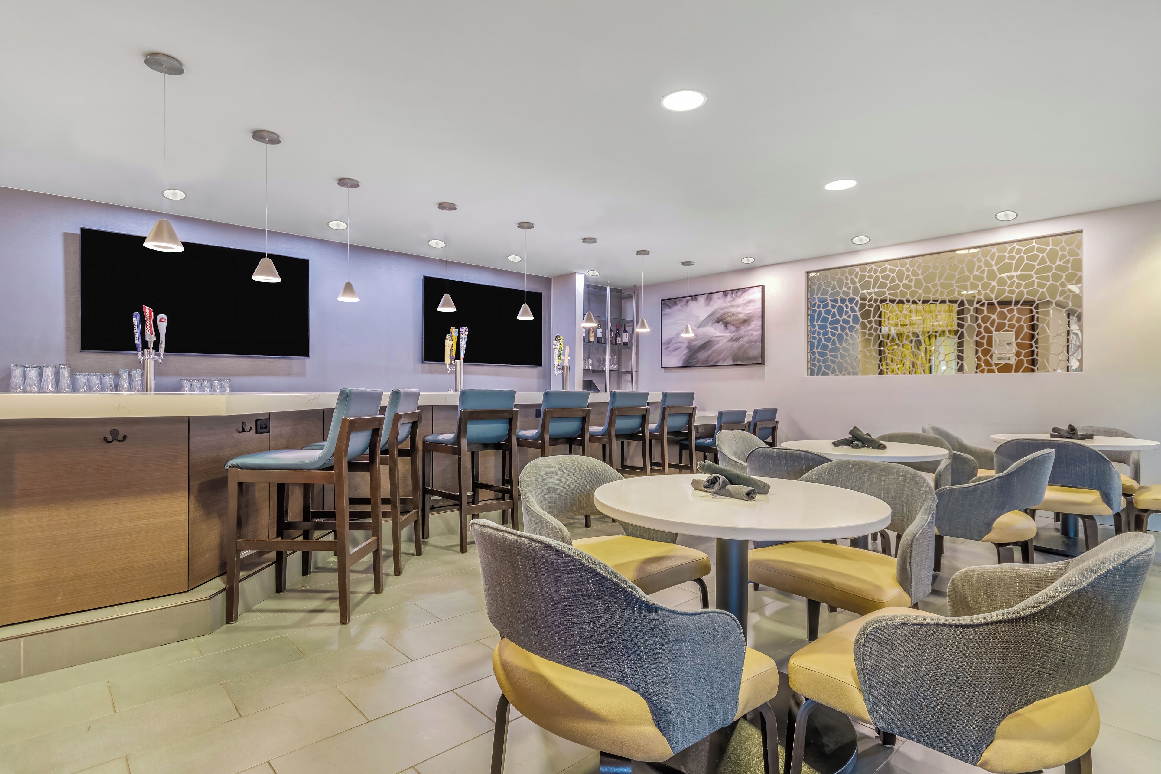 A modern restaurant interior with multiple tables and chairs, a bar area, and artwork on the walls.
