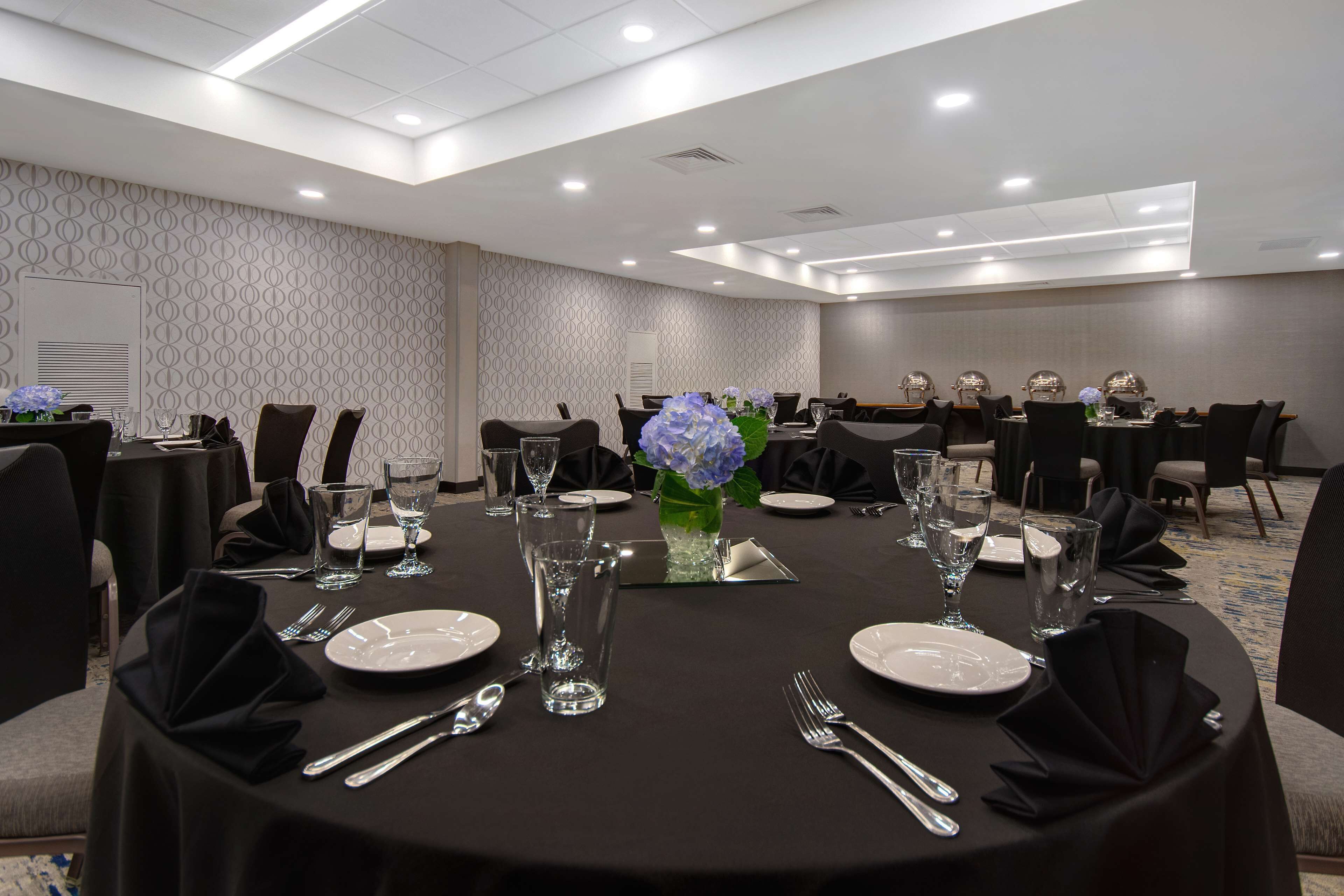 A conference room with round tables set for a meeting, equipped with chairs, plates, cutlery, and glassware.