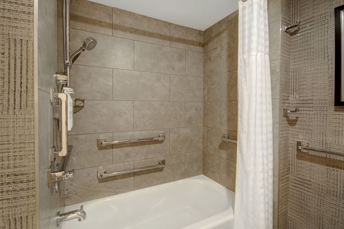 Ein Badezimmer mit Badewanne, Dusche und Haltegriffen.