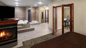 A hotel room with a fireplace, a television, a dining area with a table and chairs, and a shower area.