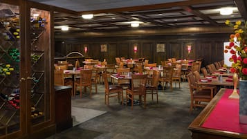 A banquet hall with wooden tables and chairs, a wine rack, and a red carpet runner.
