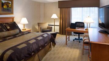 A hotel room with a large bed, a desk with a chair, a television, and two lamps.