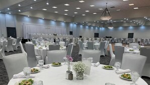 A banquet hall with round tables set for dining, white tablecloths, and chairs.
