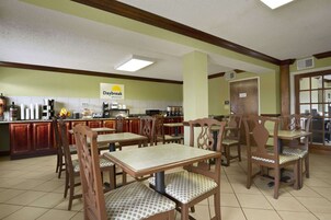 Un área de desayuno con mesas y sillas de madera, una cocina al fondo y un letrero que dice 'Daybreak Breakfast'.
