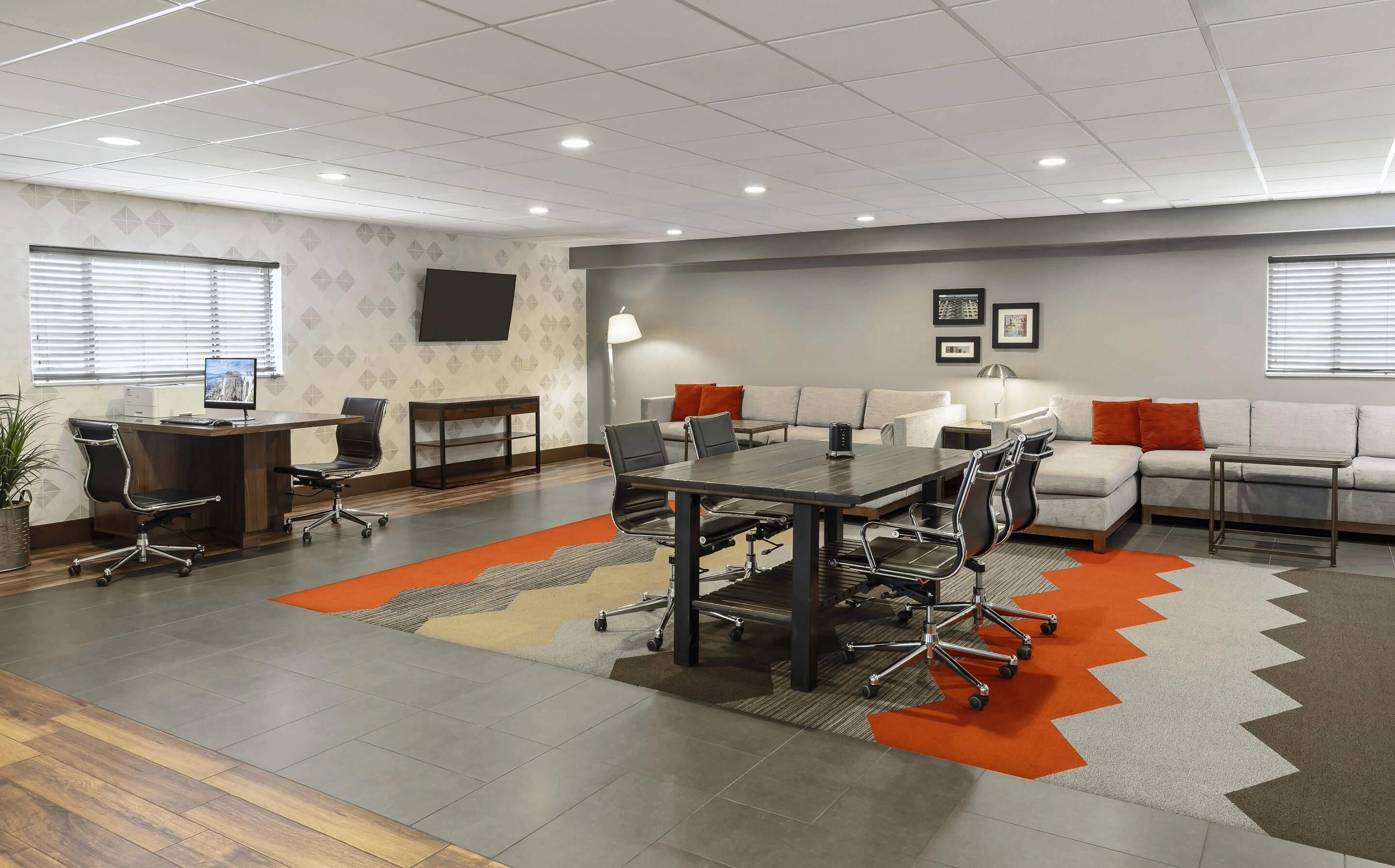 A modern conference room with a large table, chairs, a sofa, and a TV on the wall.