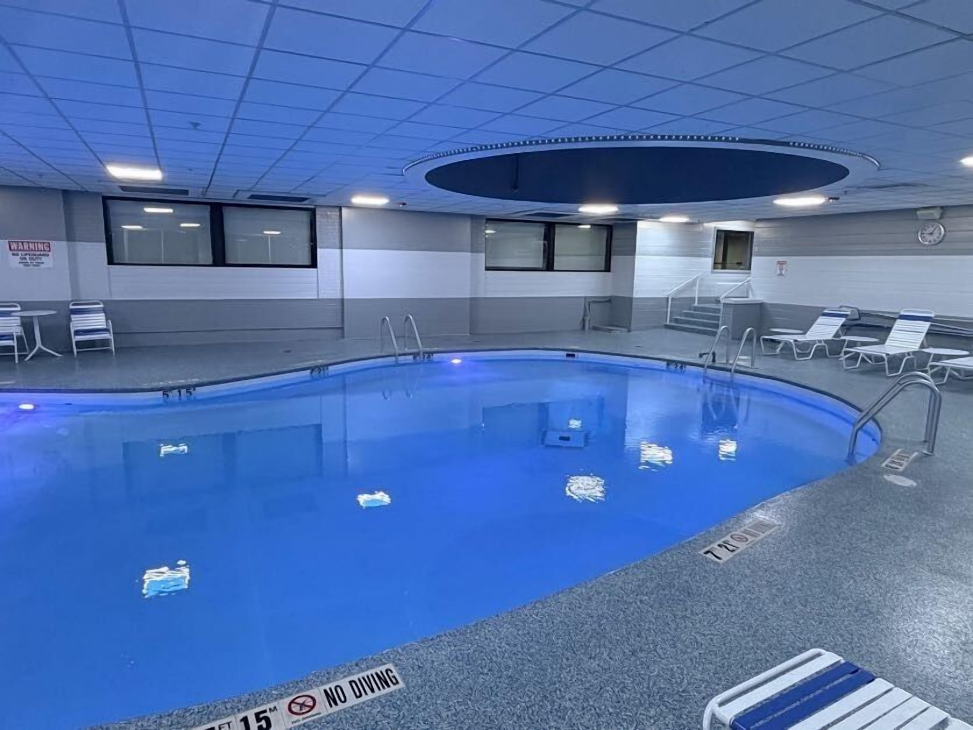 A swimming pool with a no diving sign, lounge chairs, and a clock on the wall.