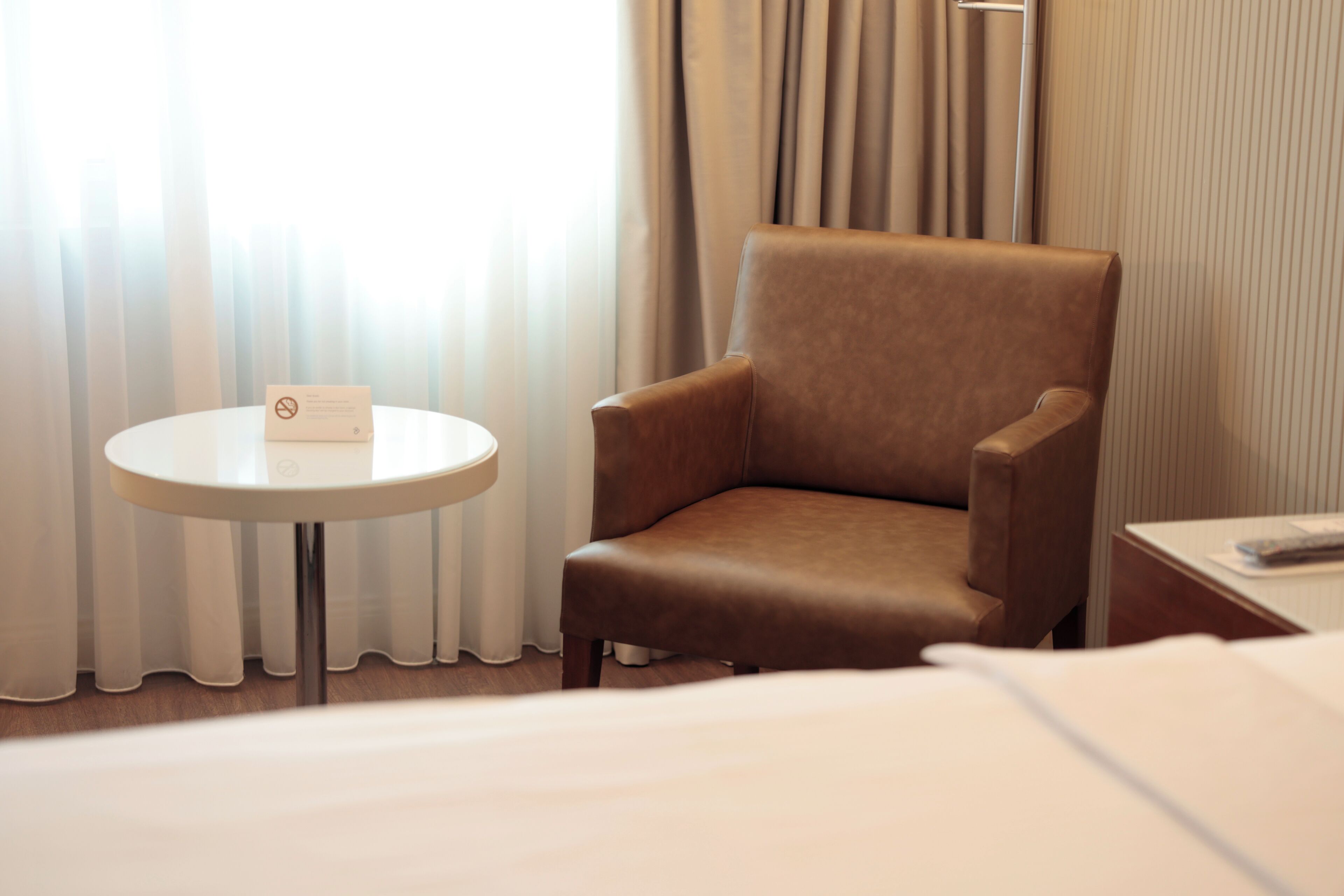 A hotel room with a brown armchair, a round table with a sign, and a bed.