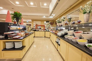A buffet area with multiple food stations, including bowls of various dishes, and decorative elements like potted plants and a Christmas tree.