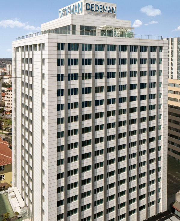 A high-rise building with a grid of windows and a sign reading "DEDEMAN" at the top.