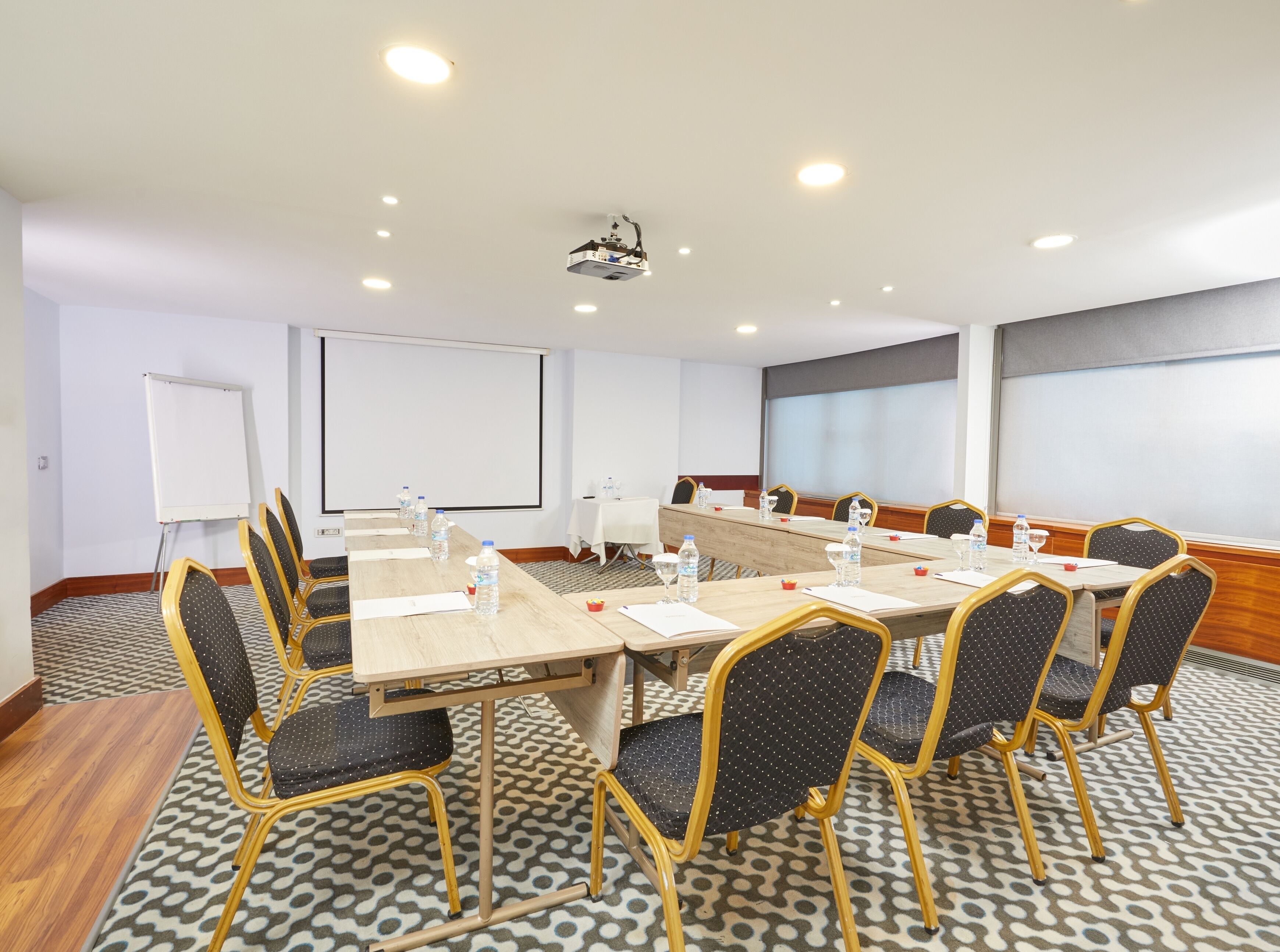 Un salón de conferencias con una larga mesa, sillas, un proyector y una pizarra.