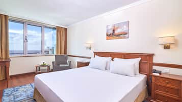 Ein Hotelzimmer mit einem großen Bett, einem Sessel, einem kleinen Tisch, einem Nachttisch und einem Gemälde an der Wand.