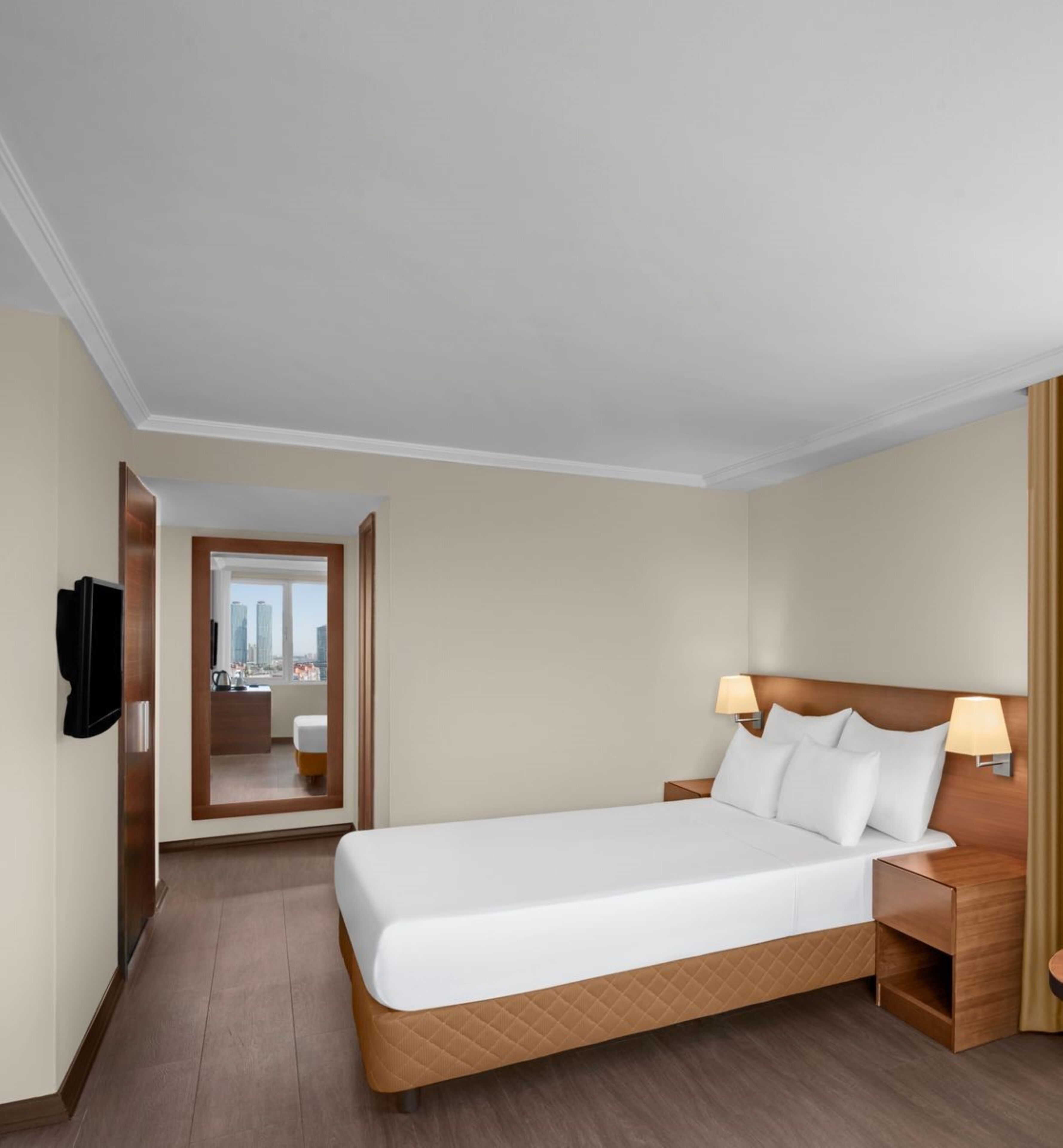 Habitación de hotel con una cama grande, lámparas de noche, cabecera de madera, mesita de noche y televisor montado en la pared.