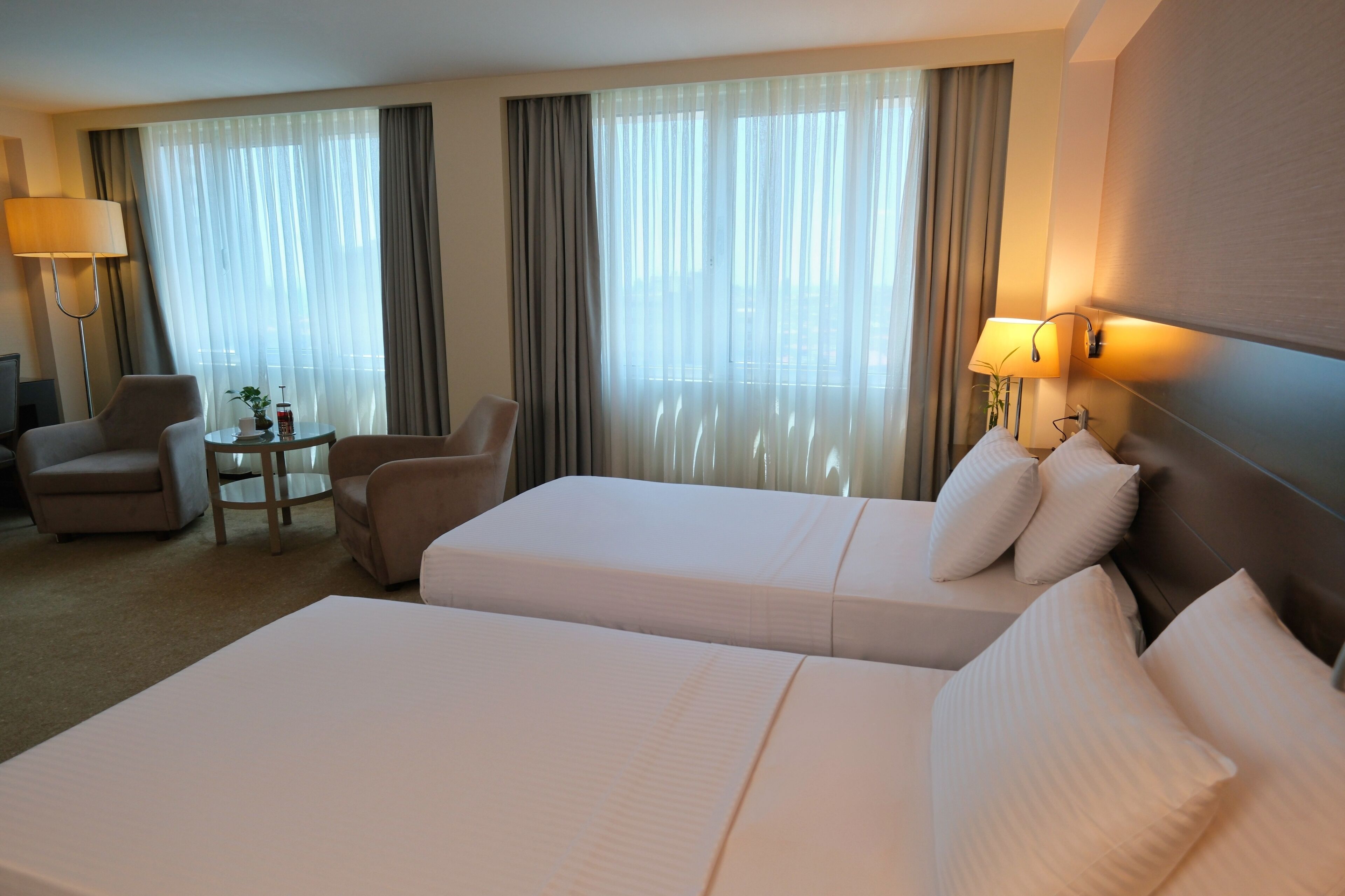 Ein Hotelzimmer mit zwei Betten, einem kleinen Tisch, zwei Stühlen und einer Lampe.