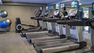 A gym with multiple treadmills, exercise balls, and televisions mounted on the walls.