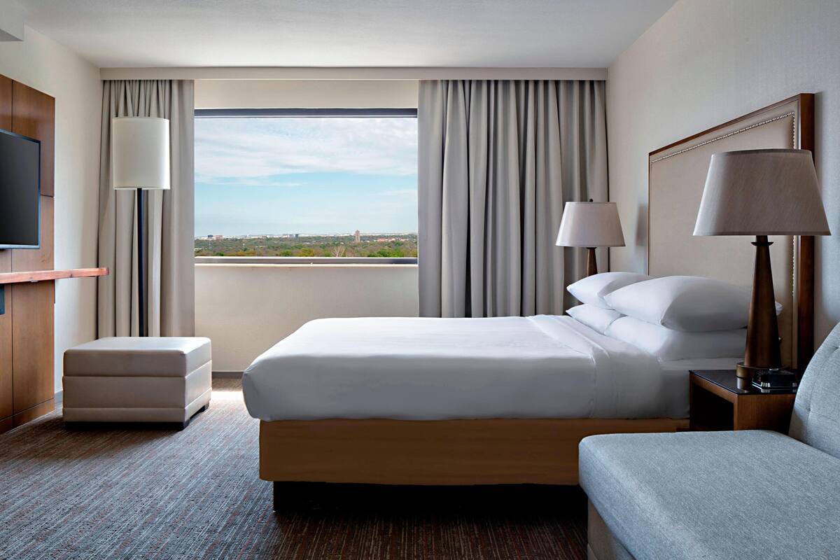 Habitación de hotel con una cama grande, televisor, escritorio y vistas a la ciudad.