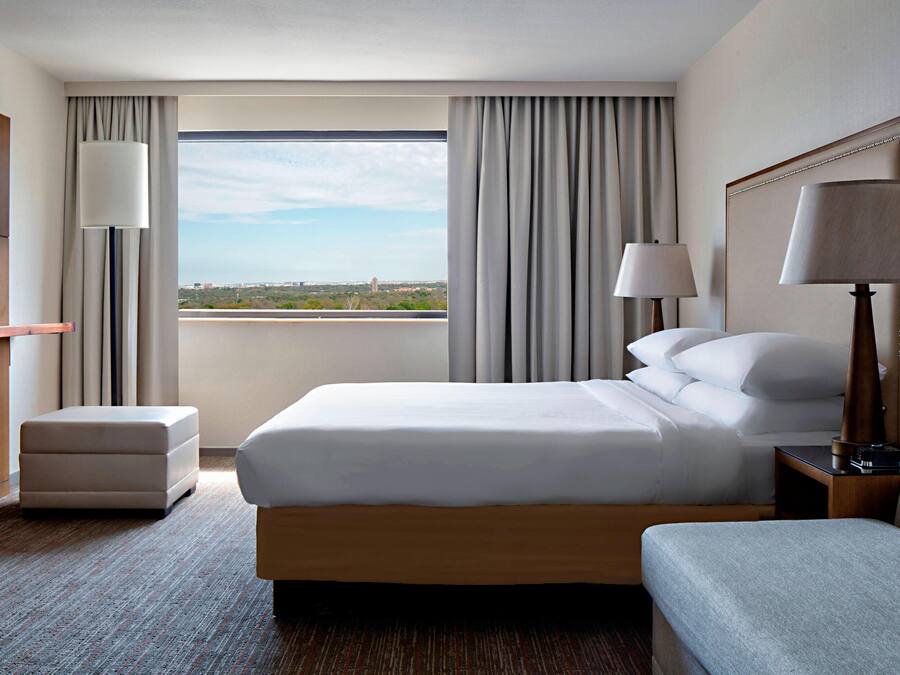 Habitación de hotel con una cama grande, televisor, escritorio y vistas a la ciudad.