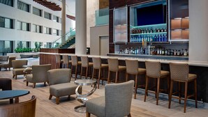 A modern bar area with multiple seating options, a staircase, and a view of the building's exterior. - San Antonio Marriott Northwest Medical Center (San Antonio)