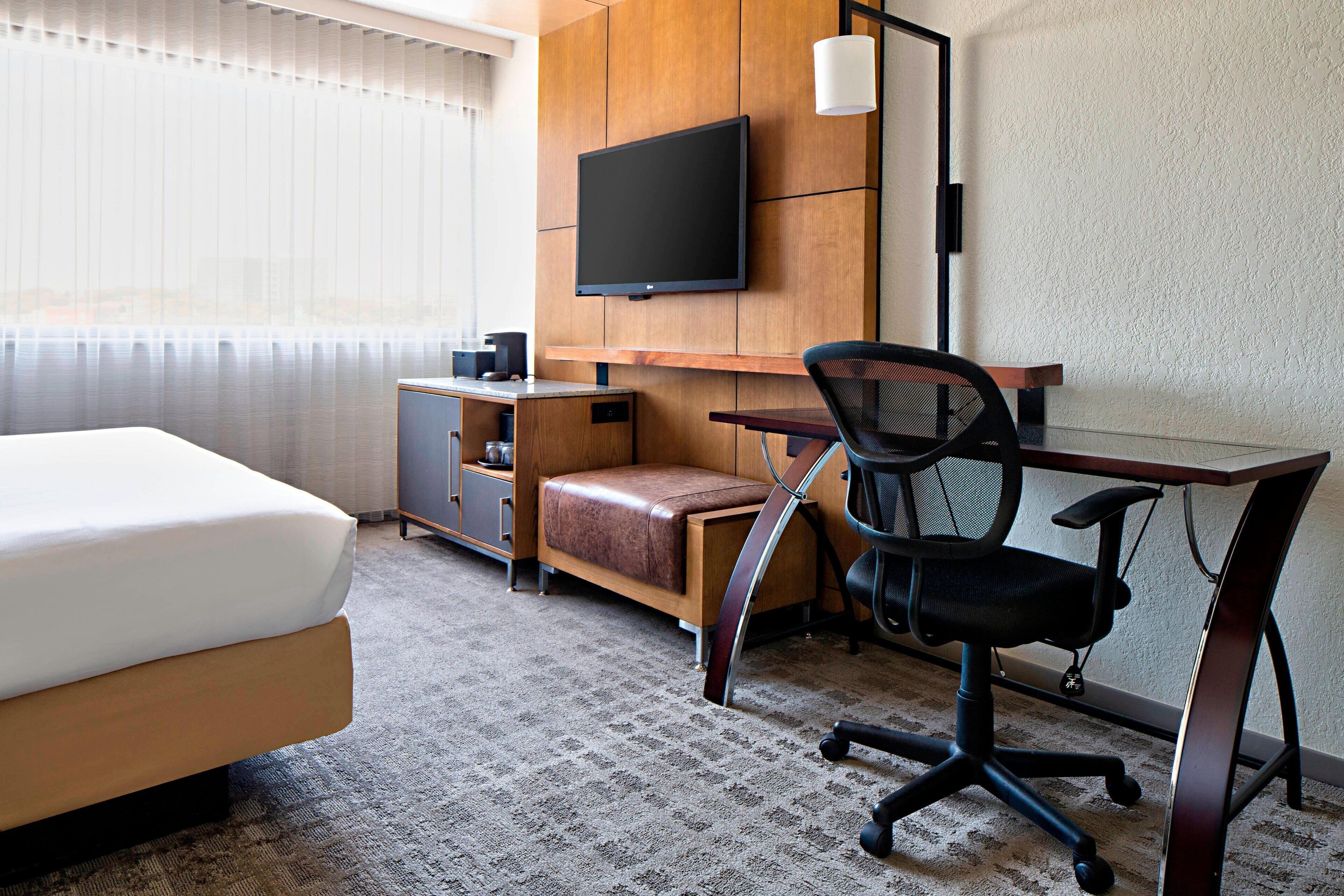 Habitación de hotel con una cama, un escritorio con una silla, un televisor y un mueble bajo.