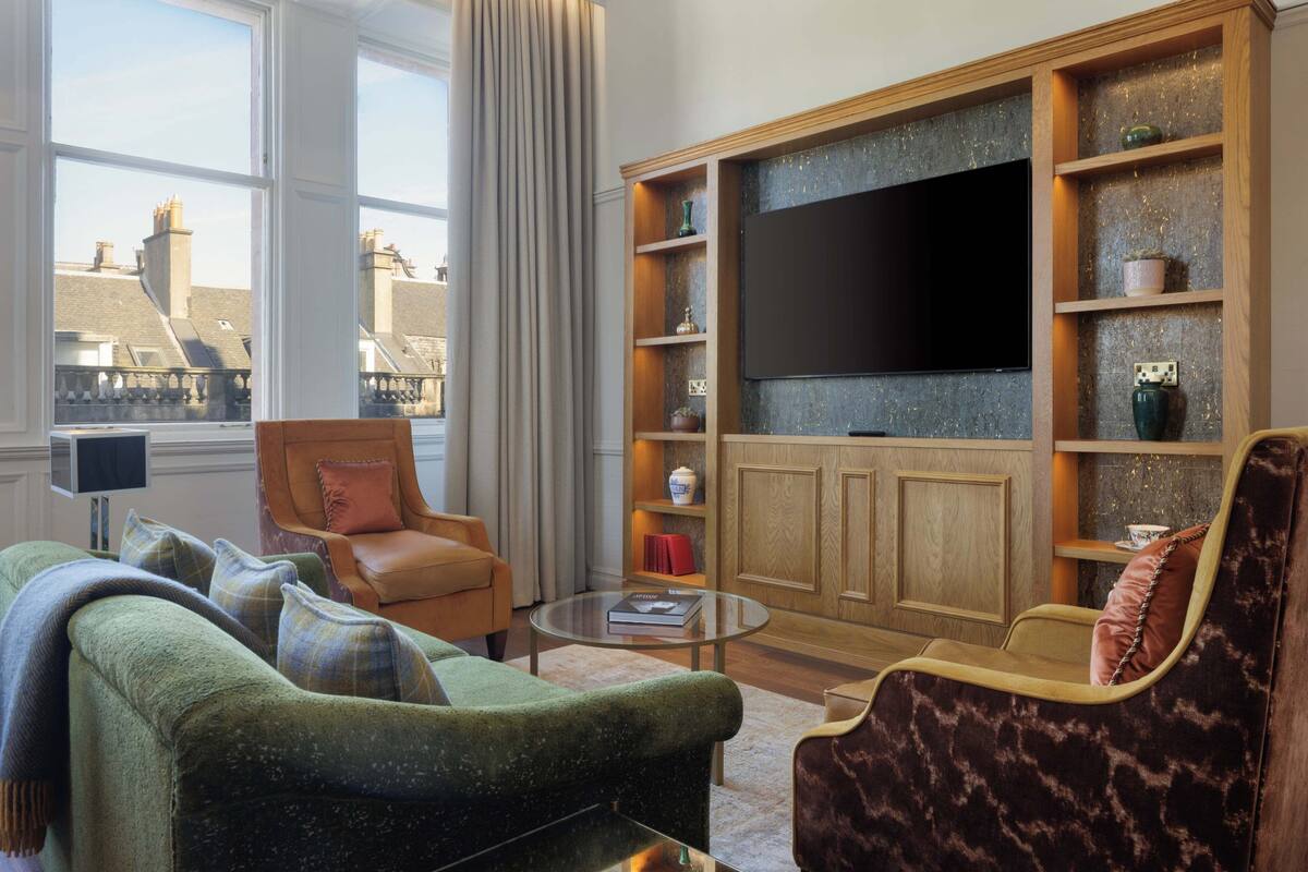 A living room with a large flat-screen TV, a green sofa, a brown armchair, and a glass coffee table.