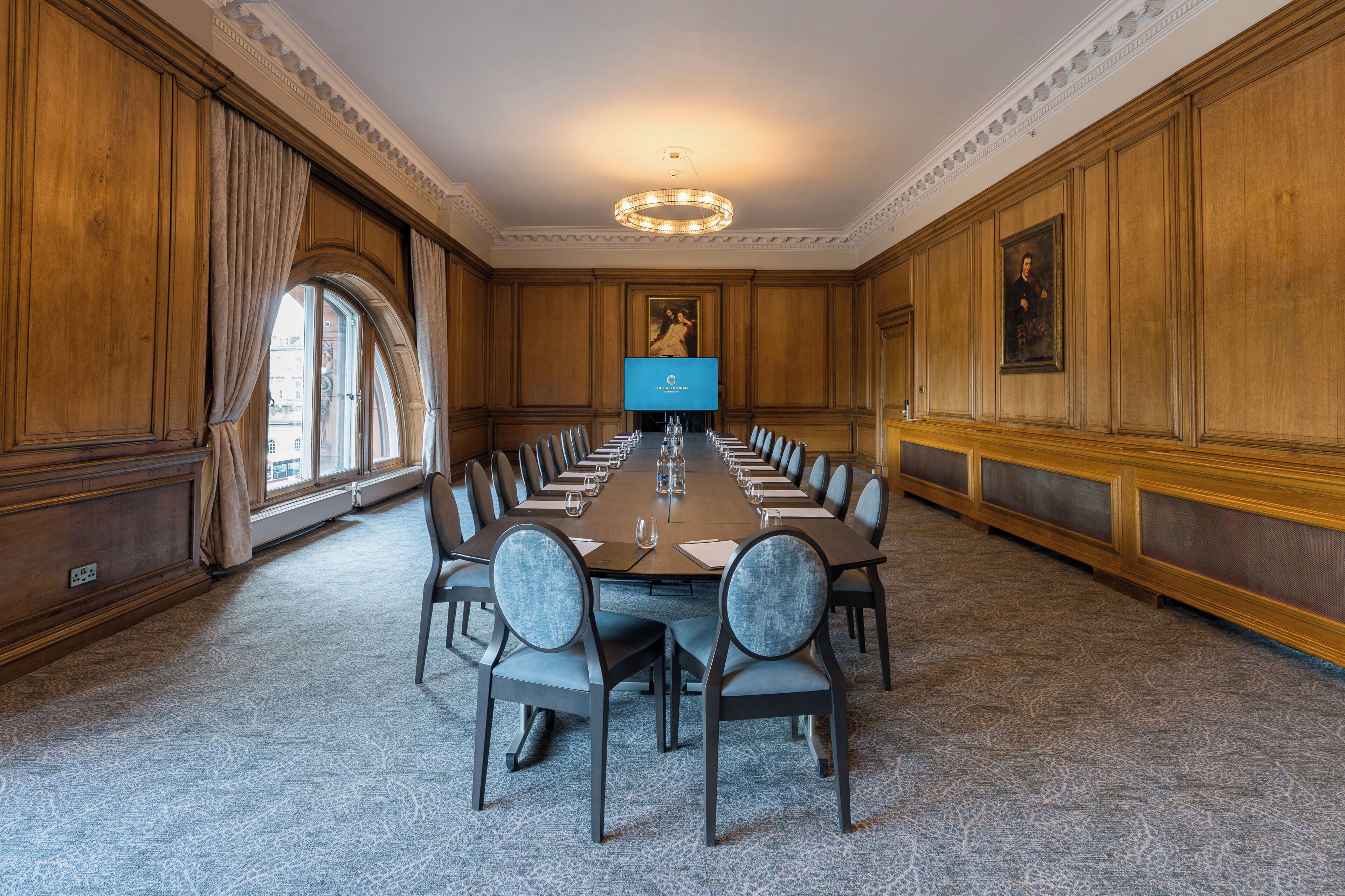 A conference room with a long table, chairs, a TV screen, and a painting on the wall.