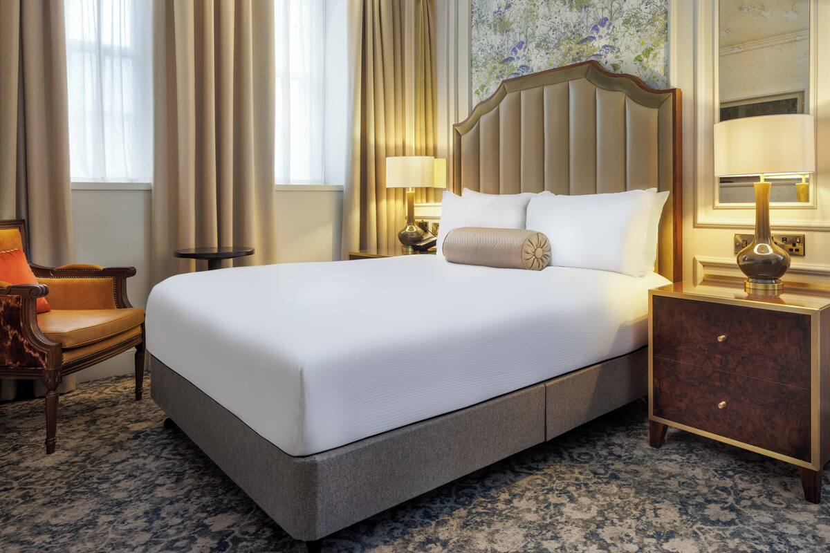 A hotel room with a large bed, a nightstand with a lamp, a chair, and a carpeted floor.