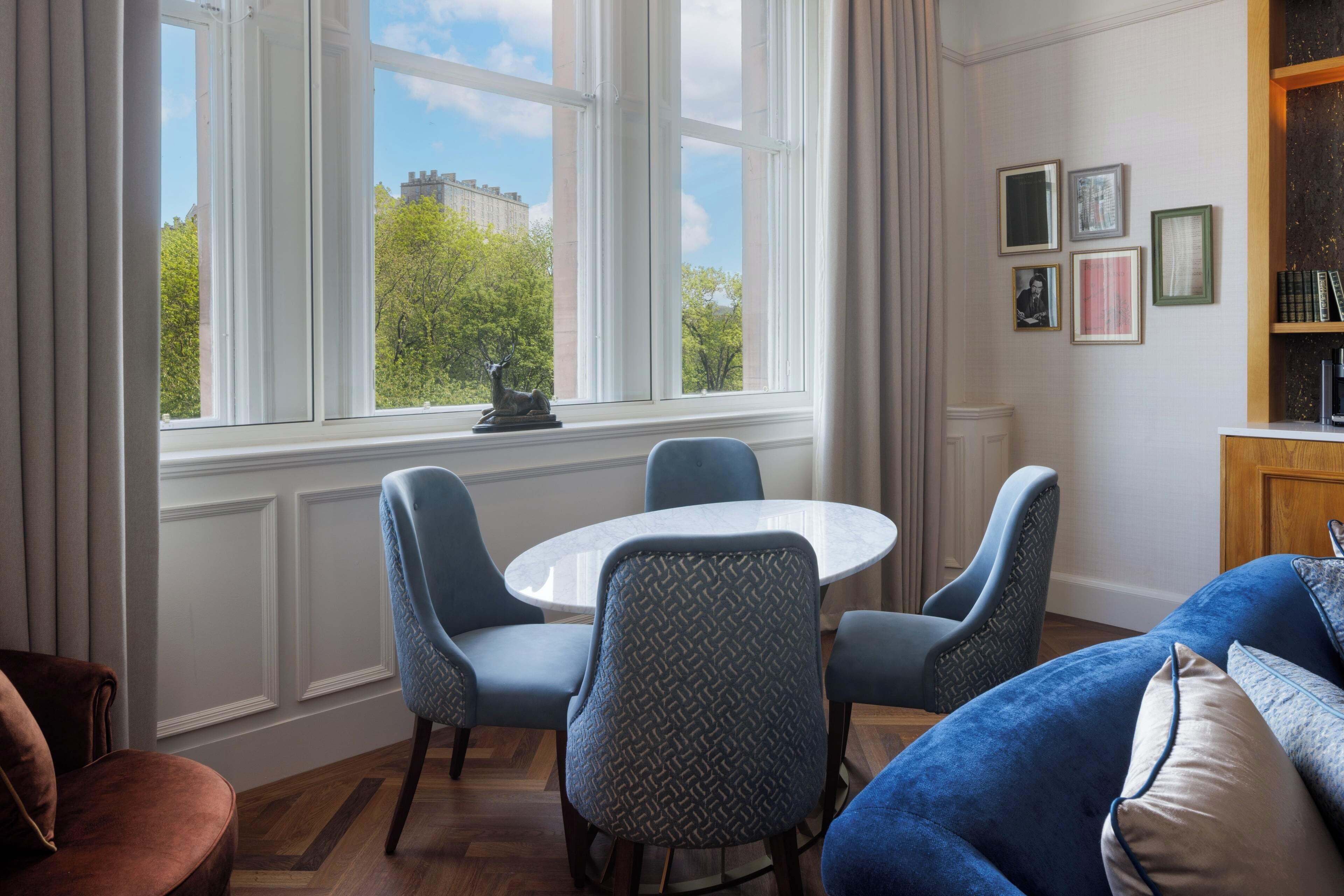 Una habitación con una mesa redonda, cuatro sillas, un sofá azul y una estantería.