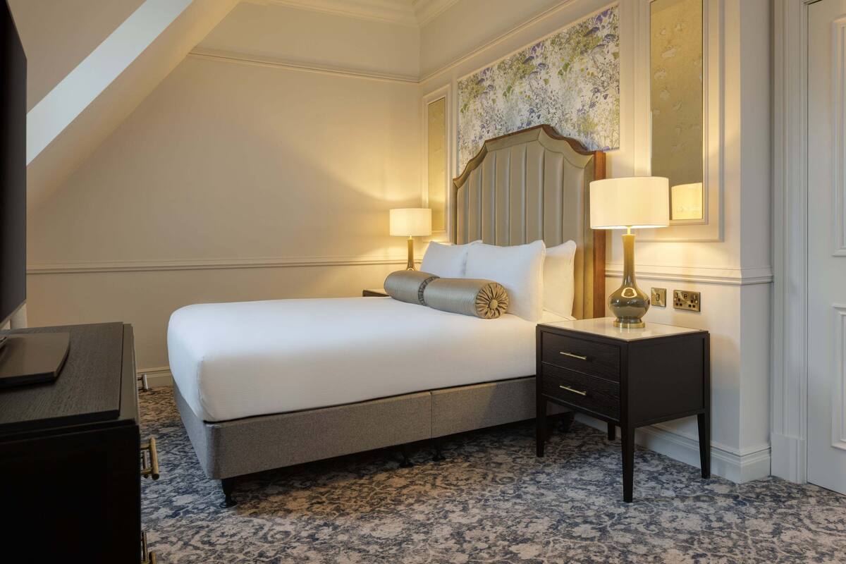 A hotel room with a large bed, a nightstand, a lamp, and a decorative headboard.