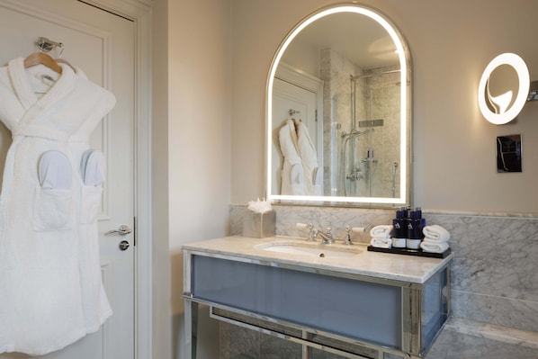 A modern bathroom with a large mirror, a sink, and a shower. There are towels and toiletries on the counter. - The Caledonian Edinburgh, Curio Collection by Hilton (Edinburgh)