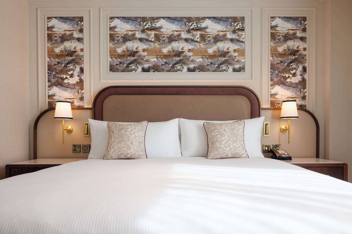 A hotel room with a large bed, two bedside lamps, and three framed artworks on the wall.
