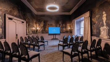 A conference room with a large screen, rows of chairs, and classical artwork on the walls.
