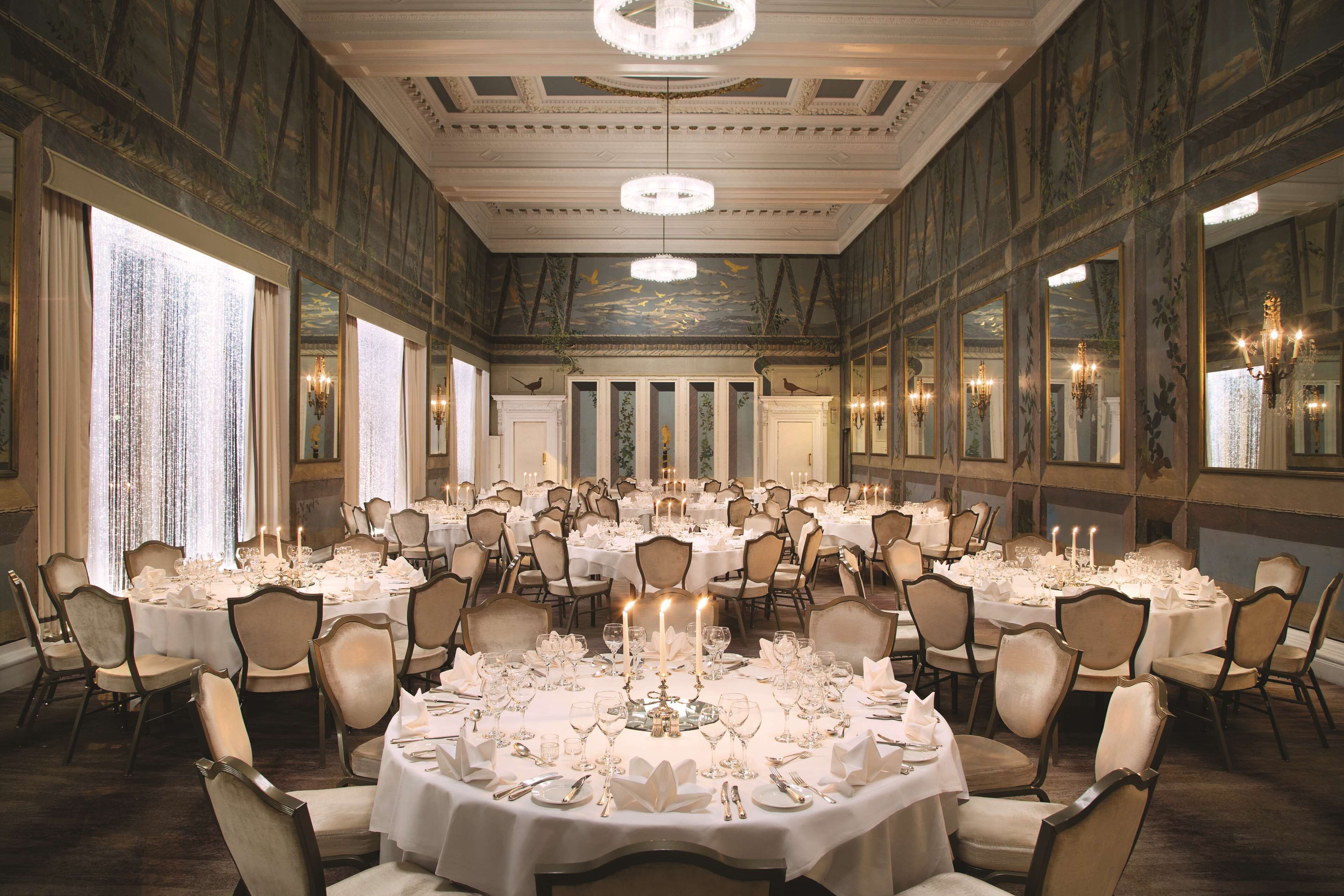 Un salón de banquetes con mesas redondas dispuestas para un evento formal, con candelabros y apliques en las paredes.